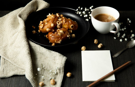 donuts with caramel and hazelnuts, cup of coffee on the rustic table, paper and pancil copy space