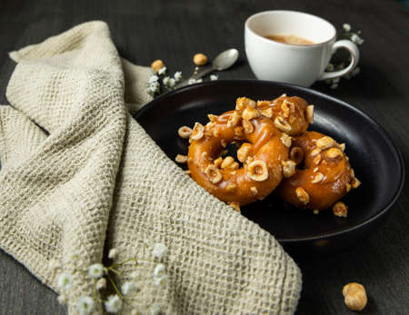 Donuts with caramel and hazelnuts, black coffee over rustic background.の写真素材
