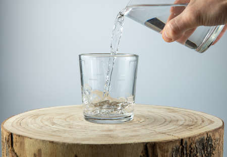 water pouring into glass on white background, wooden tableの写真素材