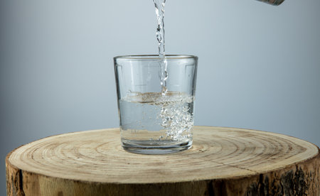 water pouring into glass on white background, wooden tableの写真素材