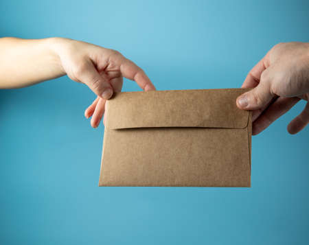 passing an envelope from hand to hand on blue background copy spaceの写真素材