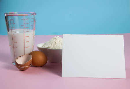 Ingredients for baking - eggs, flour, milk on a light blue and pink background with copy space for recipeの写真素材