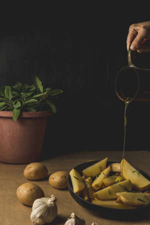 Potato wedges on dark background, cooking process. Process of making a rustic recipe of aromatic baked potatoes. Cheap and easy home cooking.の写真素材