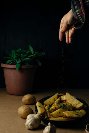 Potato wedges on dark background, cooking process. Process of making a rustic recipe of aromatic baked potatoes. Cheap and easy home cooking.の写真素材