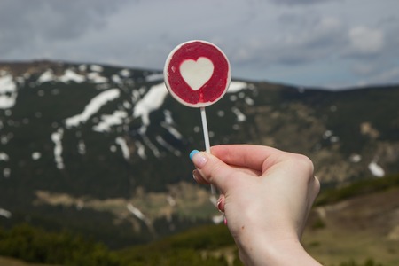 lollipop patterned heart in hand woman against  of the mountainsの写真素材