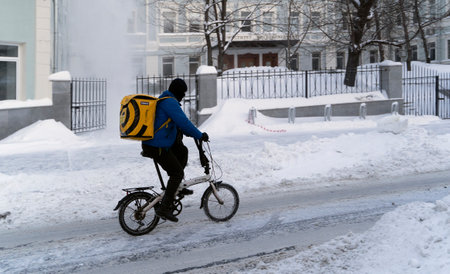 Russia, Moscow, February 14, 2021, a food delivery service rides a bicycle through the snowのeditorial素材