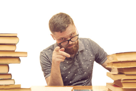 a young man with a beard in glasses at a desk between books shows a finger