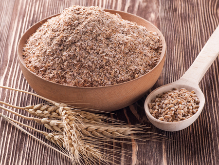 Wheat bran in wooden bowl and ears of wheat on a wooden tableの写真素材