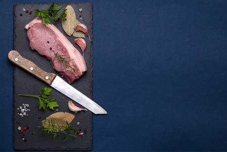 Raw pork meat on a black graphite board on a blue backgroundの写真素材