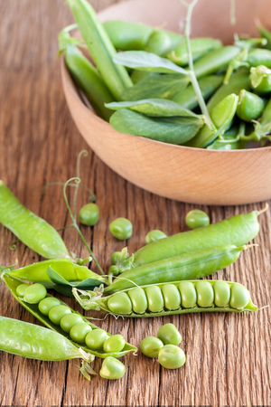 Fresh green pea in wooden bowl on old wooden background. Vegetarian food.の写真素材
