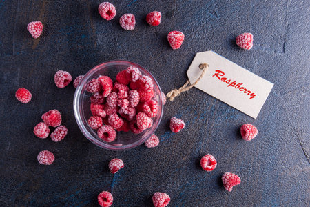 Frozen raspberries in glass bowl on vintage stone background