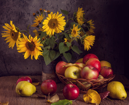 Fresh apples in basket with sunflowers on wooden table.の写真素材