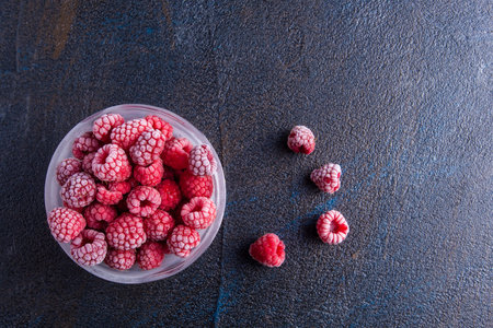 Frozen raspberries in glass bowl on vintage stone background