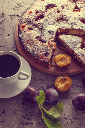 Pie with plums and cup of coffee on wooden table. Homemade traditinol food.の写真素材
