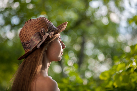 Portrait of a beautiful elegant woman in light white dress and hat standing in the summer park.の写真素材