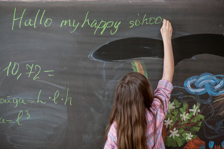 Cute girl schoolgirl near blackboard with chalk in hand,the concept of education and school lifeの写真素材