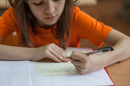 Little girl writing something in copybook and sitting at tableの写真素材