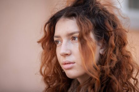 Dreaming young woman with spectacular curly red ginger hair looking at camera posing outdoor in downtown street. Female portrait.の写真素材