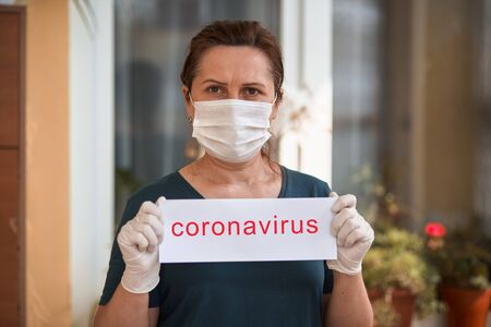 Woman in medical mask holding card with coronavirus lettering. Covid-19.の写真素材