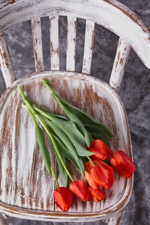 red tulips on a wooden vintage old white chairの写真素材