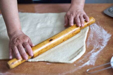 Women's hands roll the dough on the kitchen table. Women's hands with rolling pinの写真素材