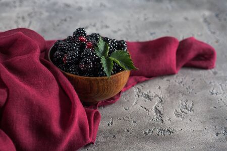 Sweet blackberry and leaves in wooden bowl on grey stone background.の写真素材