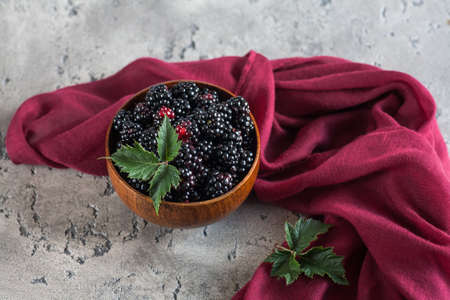 Sweet blackberry and leaves in wooden bowl on grey stone background. Top view.の写真素材