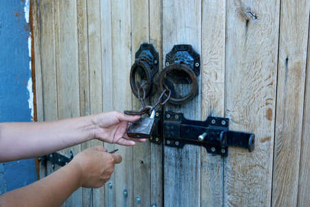 Women opens an ancient wooden door decorated with wrought iron elements. Old lock with an iron handle. Close-up. Selective focus.の写真素材