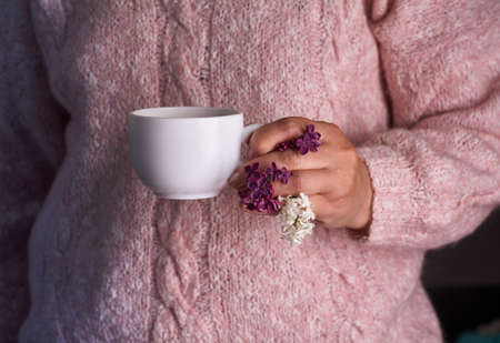 Woman's hand holding a white cup of coffee. With a beautiful lilac flowers. Drink, fashion, morningの写真素材