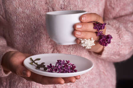 Woman's hand holding a white cup of coffee. With a beautiful lilac flowers. Drink, fashion, morningの写真素材