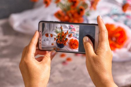 The hand holds the phone and photographs the still life of the poppies