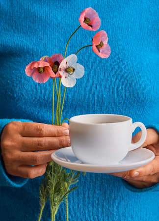 Girl holding poppy flowers and a White cup of warm morning coffee. Blue background.の写真素材