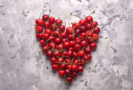 Ripe red cherries on gray background arranged in the shape of a heartの写真素材