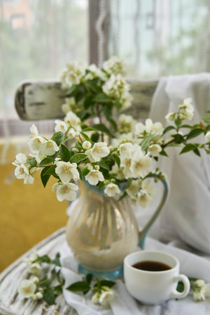 Jasmine flowers in a white vase. Stillife with jasmine and cup of coffee.