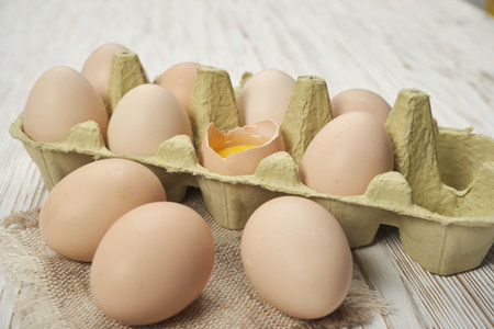Close-up view of raw chicken eggs in egg box on wooden background. Raw chicken eggs in egg box...