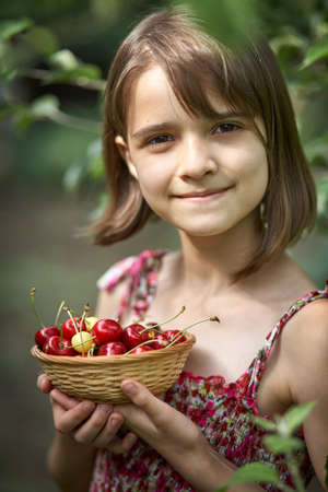 Beautiful girl holding a bowl of cherries in the gardenの写真素材