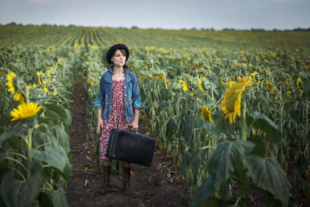 Cute girl with old suitcase in a sunflower field.の写真素材