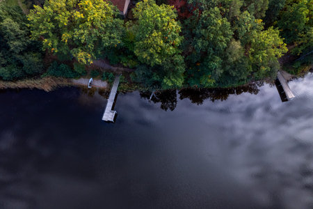 A drone flies over a huge blue lake with a wooden pier among the forests on a cloudless autumn day...