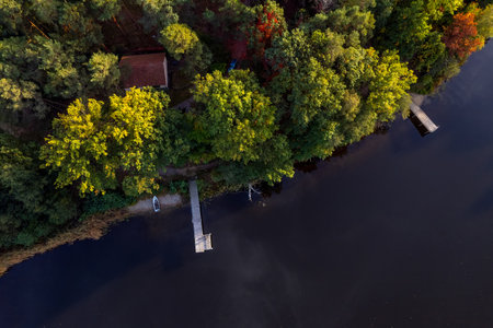 A drone flies over a huge blue lake with a wooden pier among the forests on a cloudless autumn day at dawn.の写真素材