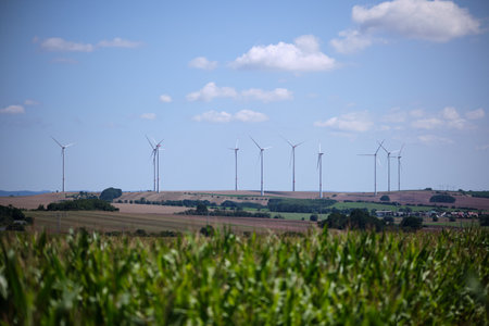 Green cornfield and wind power turbine against a blue sky with white clouds. Renewable energy source. Powerful and ecological energy conceptの写真素材