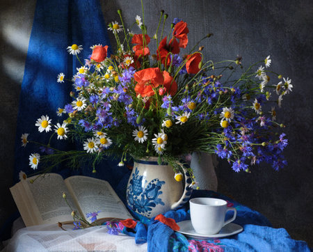 A beautifully arranged bouquet of vibrant wildflowers positioned beside an elegant tea cup and an open bookの写真素材
