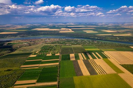A breathtaking aerial shot captures the vibrant green fields and a meandering river flowing beneath a clear blue skyの写真素材