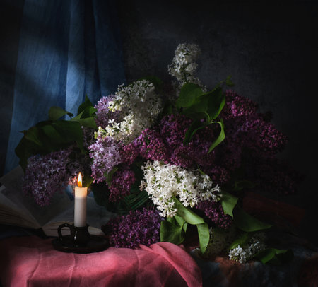 A delightful and charming arrangement of fragrant lilacs placed in a vintage jug next to books, candle and colorful fabricの写真素材