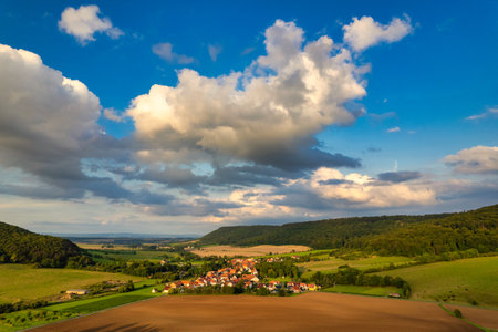 Charming german sprawling villages across a lush valley, with vibrant rooftops dotting the landscape under a blue sky adorned with fluffy clouds. Nature thrives in every direction. Germany.の写真素材