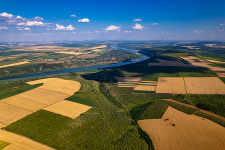 A breathtaking aerial shot captures the vibrant green fields and a meandering river flowing beneath a clear blue skyの写真素材