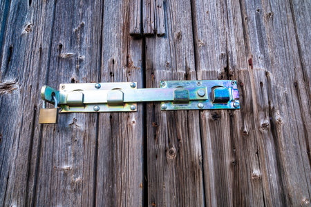 An aged wooden door with rustic metal hinges and deep weathered texture. Old wooden door with lock.の写真素材