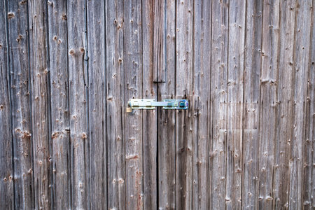 An aged wooden door with rustic metal hinges and deep weathered texture. Old wooden door with lock.の写真素材