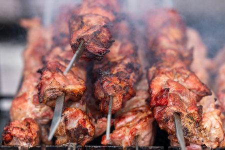 Charred shashlik skewers sizzling over grill, late-night market mood, smoky aroma, ember glow, rich marinadeの写真素材