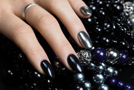 Beautiful female hands with nail polish black and silver color with black and silver beads on a black backgroundの写真素材