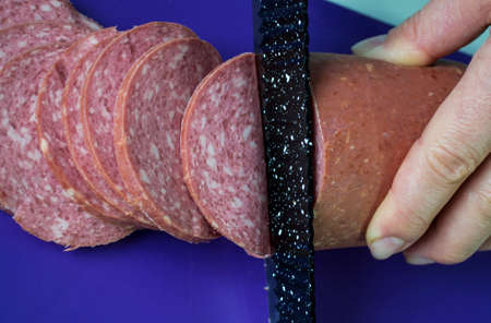 Slicing a sausage loaf with a black knife.の写真素材